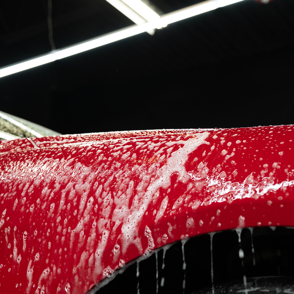 Red car exterior covered in soap suds. Car detailing and auto care services.